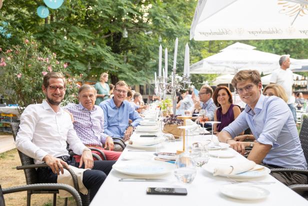 Eine Gruppe von Menschen sitzt an einem langen, gedeckten Tisch im Freien.
