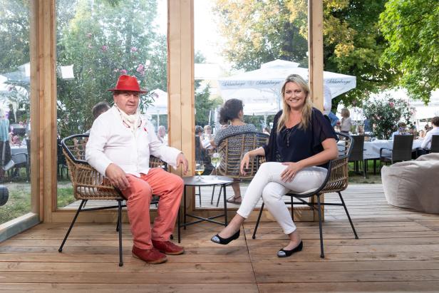 Ein Mann mit rotem Hut und eine Frau sitzen auf Stühlen im Freien.