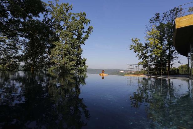 Eine Frau schwimmt in einem Infinity-Pool mit Blick auf eine grüne Landschaft.