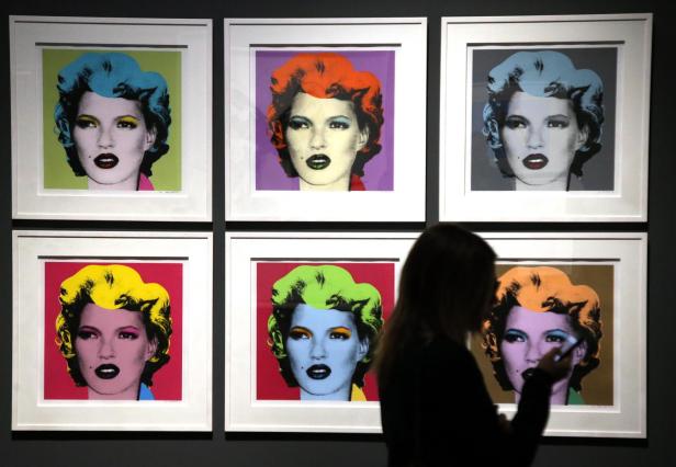 Eine Frau betrachtet an einer Wand hängende, farbenfrohe Porträts von Kate Moss.
