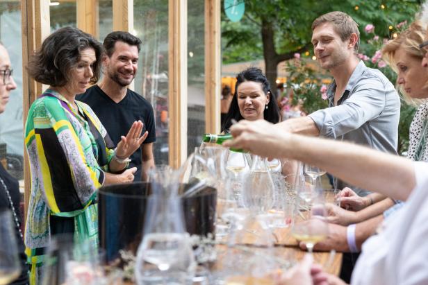 Eine Gruppe von Menschen steht an einem Tisch, an dem Wein eingeschenkt wird.