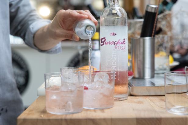 Eine Person gießt Soda in Gläser mit Eis und „Burschik Rose“ Vermouth.