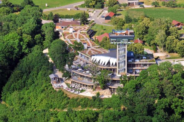 Luftaufnahme eines modernen Hotels mit begrünten Dächern und einem Aussichtsturm inmitten von Bäumen.
