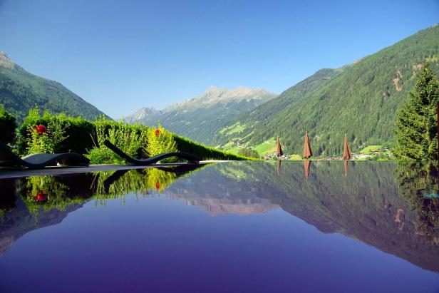 Ein Infinity-Pool spiegelt die umliegenden Berge und den blauen Himmel wider.