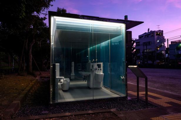 Eine öffentliche Toilette mit Glaswänden in einem Park bei Dämmerung.