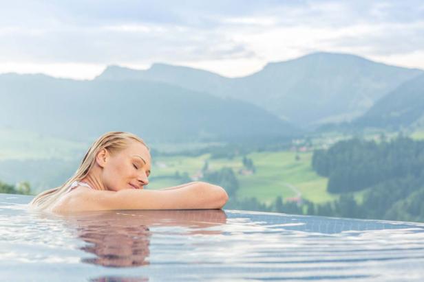 Eine Frau entspannt in einem Pool mit Blick auf eine grüne Berglandschaft.