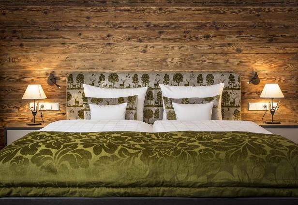 Ein Doppelbett mit grüner Tagesdecke und Holzwand im Hintergrund.