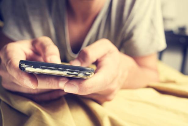 Eine Person liegt im Bett und benutzt ein Smartphone.