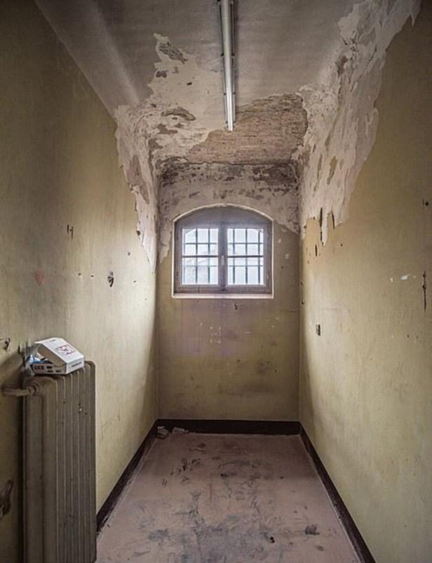 Ein schmaler, heruntergekommener Raum mit einem vergitterten Fenster und abblätternder Farbe.