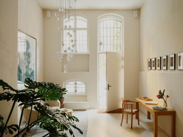 Ein helles Zimmer mit hohen Fenstern, einer modernen Lampe und Pflanzen.