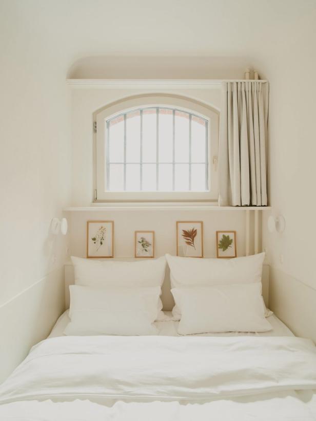 Ein minimalistisches, weißes Schlafzimmer mit einem Bett und Pflanzenbildern.