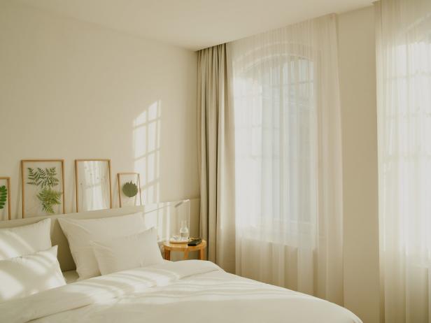 Ein helles Schlafzimmer mit weißen Kissen und Pflanzenbildern an der Wand.