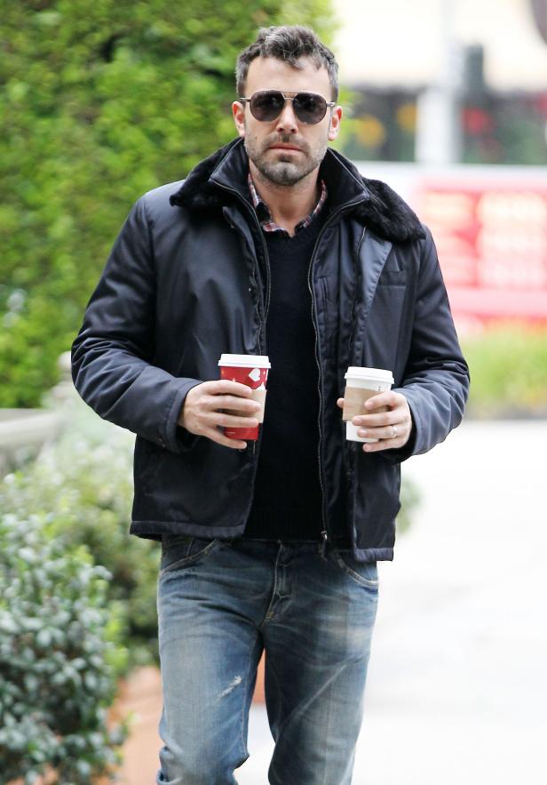 Ben Affleck geht mit zwei Kaffeebechern in der Hand die Straße entlang.