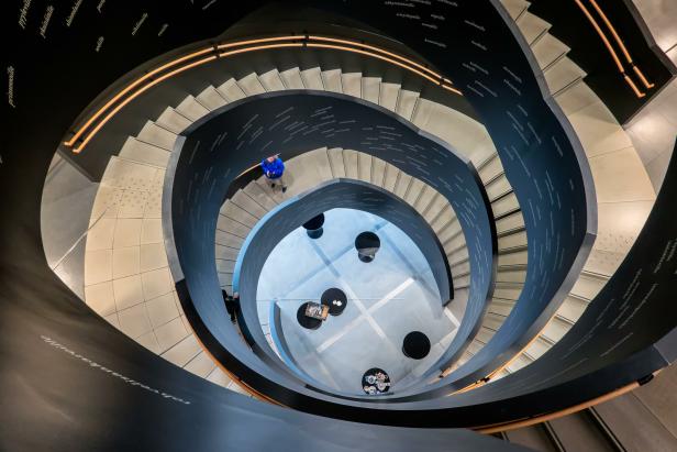 Blick von oben auf ein spiralförmiges Treppenhaus mit beschrifteten Wänden und Personen.