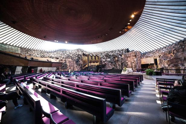 Innenansicht der Temppeliaukio-Kirche in Helsinki mit Bänken und Felswänden.