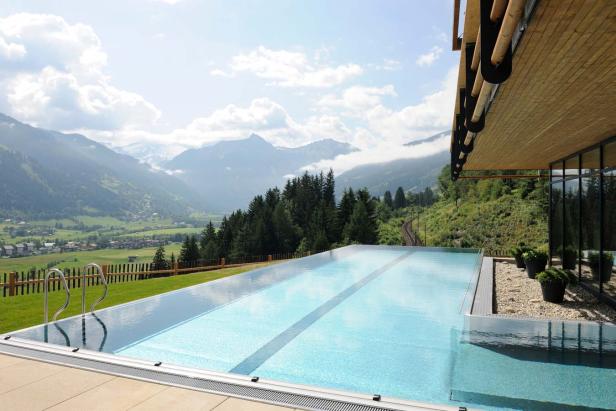 Ein Schwimmbad mit Blick auf eine grüne Landschaft und schneebedeckte Berge.