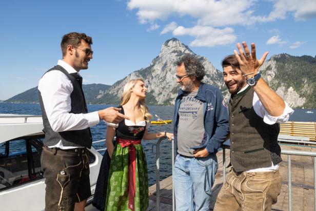 Vier Personen in Tracht stehen auf einem Boot vor dem Traunstein am Traunsee.