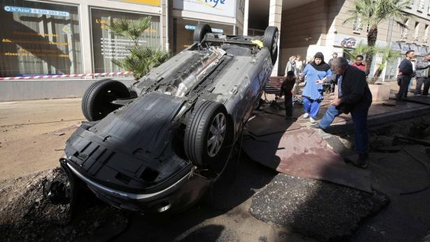 Ein Auto liegt auf dem Dach, umgeben von Trümmern und Passanten.