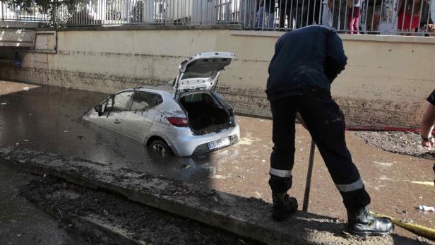 Ein Auto steht bis zur Hälfte im schlammigen Wasser, während ein Arbeiter daneben steht.