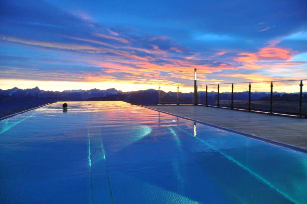 Ein Infinity-Pool spiegelt den Sonnenuntergang über den Bergen wider.