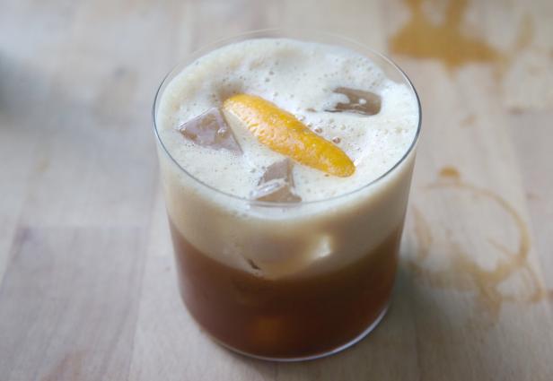 Ein Glas mit einem Nitro-Kaffee-Cocktail, Eiswürfeln und einer Orangenzeste.
