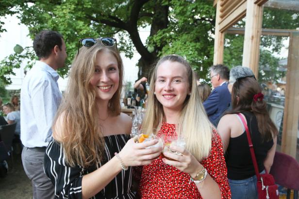 Zwei junge Frauen stoßen im Freien mit Cocktails an.