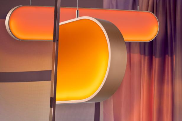 Zwei orangefarbene, moderne Lampen hängen vor einem Vorhang.
