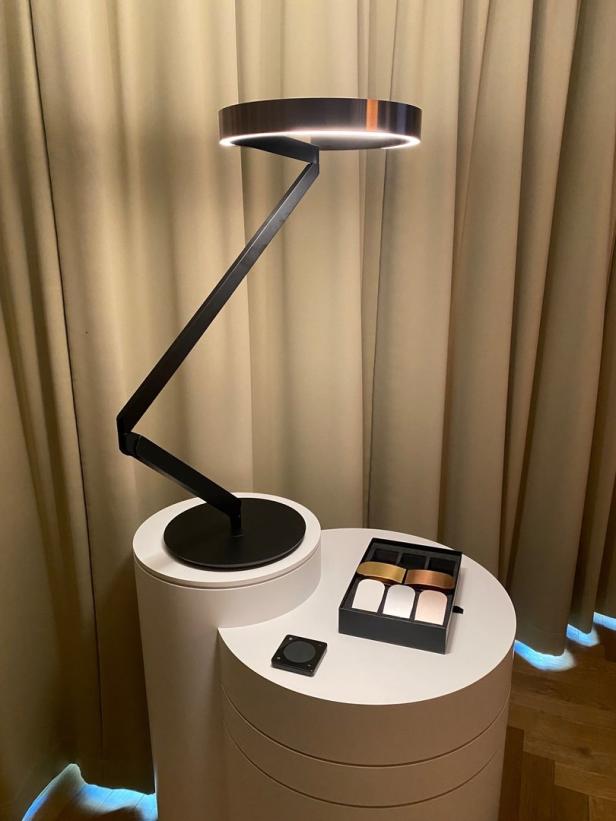 Eine moderne, schwarze Lampe steht auf einem weißen, zylindrischen Tisch.