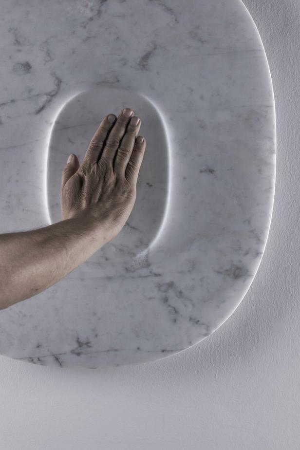 Eine Hand berührt eine kreisförmige Marmorplatte mit einer Lichtöffnung.