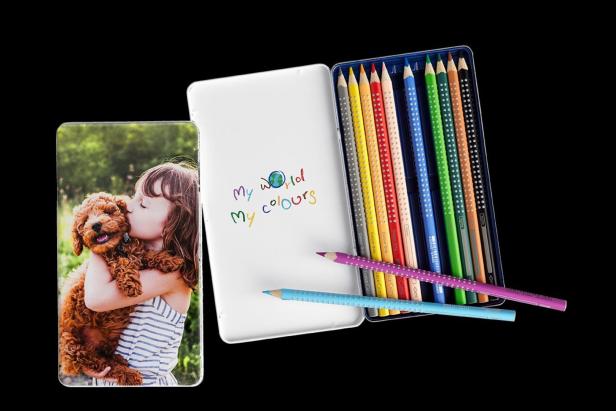 Ein Foto von einem Mädchen mit einem Hund, einer Buntstiftpackung und einer Schachtel mit der Aufschrift „My World My Colours“.