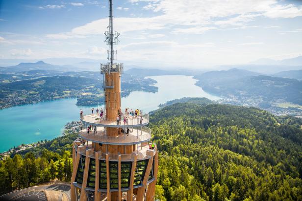 Der Aussichtsturm Pyramidenkogel in Kärnten mit Besuchern und Blick auf den Wörthersee.