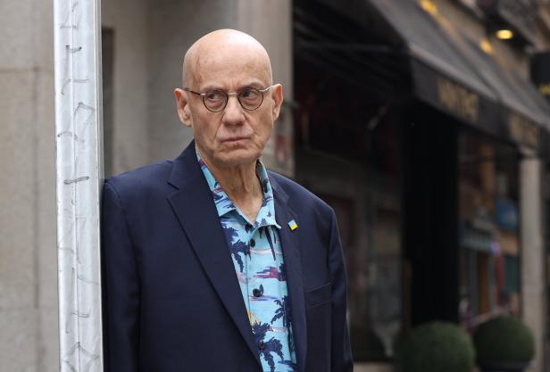 Ein Mann mit Brille und blauem Sakko lehnt an einem Pfosten.