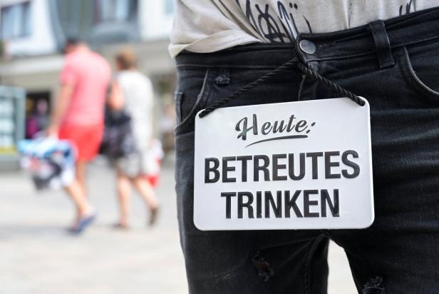 Eine Person trägt ein Schild mit der Aufschrift „Heute: Betreutes Trinken“.
