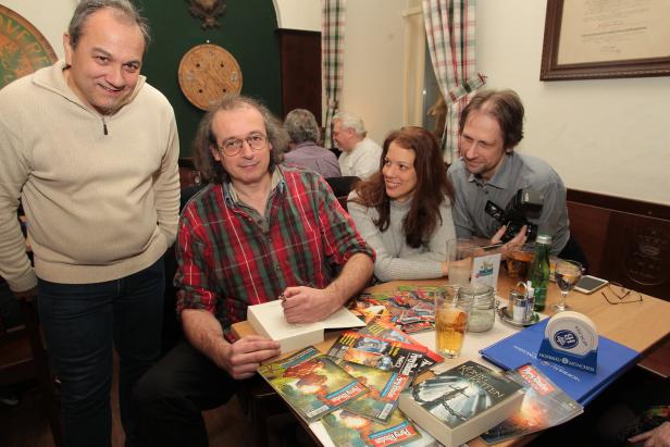 Ein Mann signiert ein Buch am Tisch, umgeben von anderen Personen und Perry Rhodan-Magazinen.