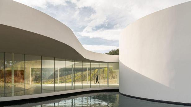 Eine Person geht durch einen gläsernen Pavillon mit Blick auf einen Weinberg.