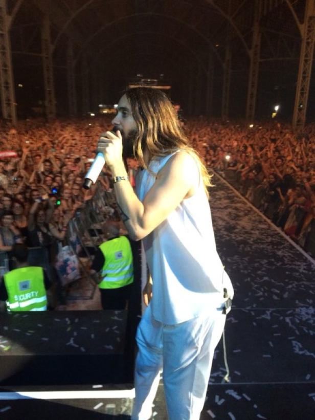 Jared Leto tritt in weißer Kleidung vor einer großen Menschenmenge auf.
