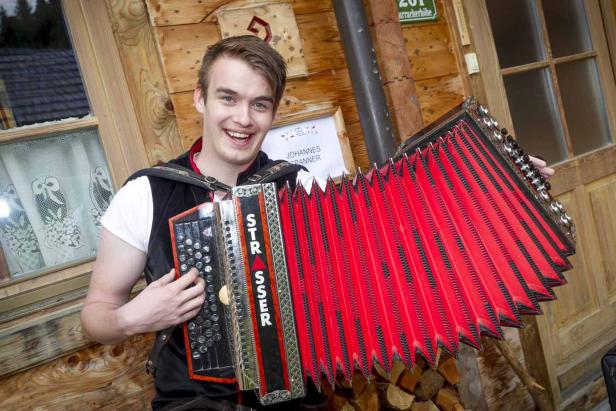 Ein junger Mann lächelt und spielt auf einer roten Steirischen Harmonika der Marke Strasser.