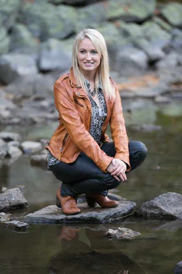 Eine blonde Frau hockt auf einem Felsen in einem Bach.