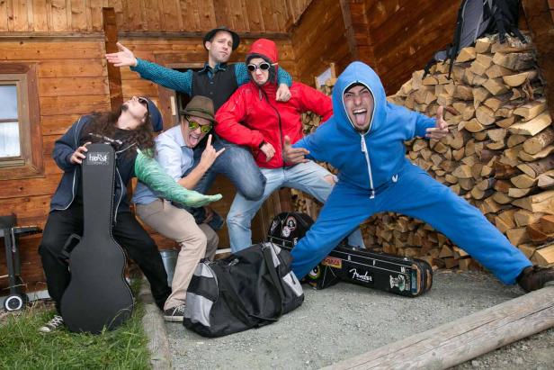 Eine Gruppe von fünf Personen posiert vor einem Holzhaus und einem Stapel Holz.