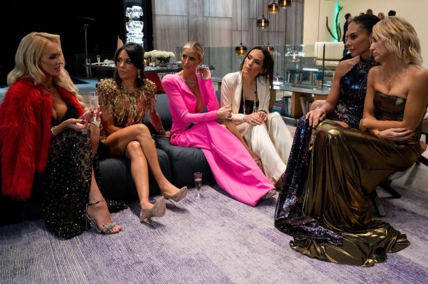 Sechs Frauen sitzen in eleganter Kleidung in einem Wohnzimmer.
