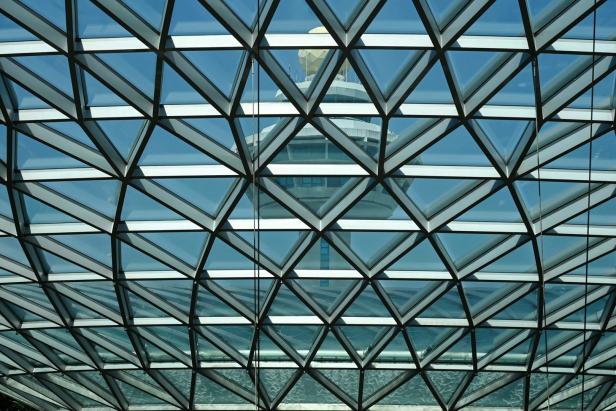 Blick durch eine Glasdachkonstruktion auf einen Turm mit Kuppel im Hintergrund.