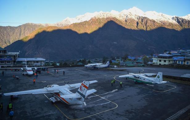 Mehrere Flugzeuge stehen auf dem Flugplatz Lukla in Nepal vor einer Bergkulisse.