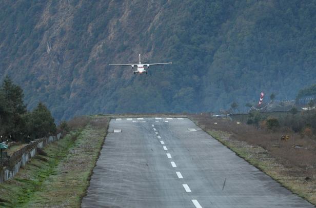 Ein Flugzeug landet auf einer Landebahn vor einer bergigen Landschaft.