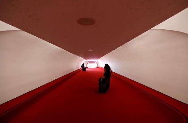 Zwei Personen ziehen Gepäck durch einen Tunnel mit rotem Teppich.