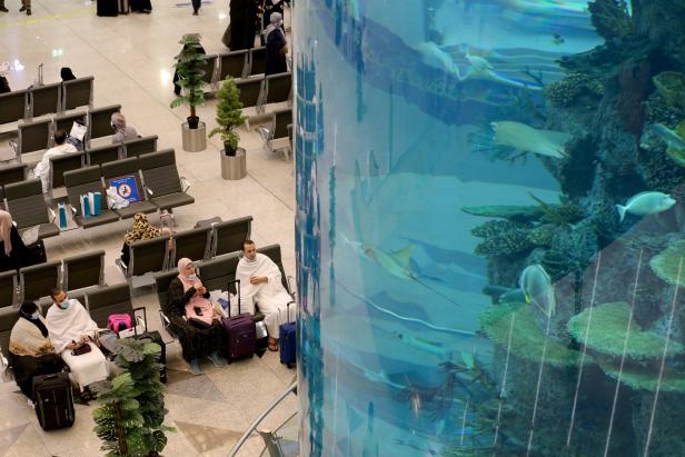 Reisende warten in einem Flughafen neben einem großen Aquarium.