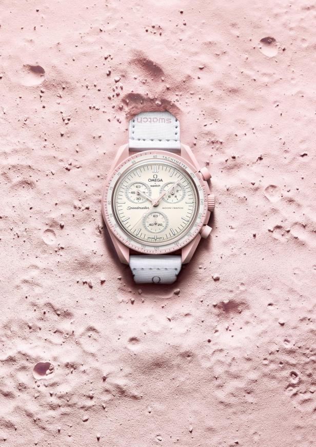 Eine rosafarbene Omega x Swatch MoonSwatch Uhr liegt auf einer rosafarbenen, kraterartigen Oberfläche.