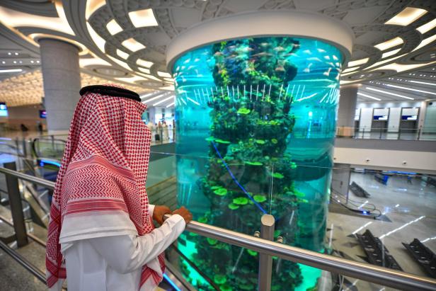 Ein Mann in traditioneller Kleidung betrachtet ein großes Aquarium in einem modernen Gebäude.