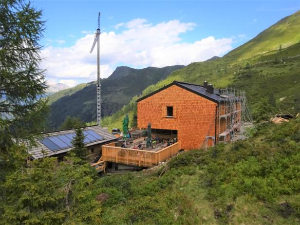 Ein Berghaus mit Terrasse und Gästen vor einer Bergkulisse.