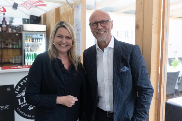 Eine Frau und ein Mann in Anzügen stehen nebeneinander und lächeln.