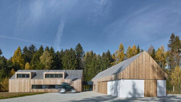 Ein modernes Holzhaus mit einem Traktor im Vordergrund vor einem Wald.